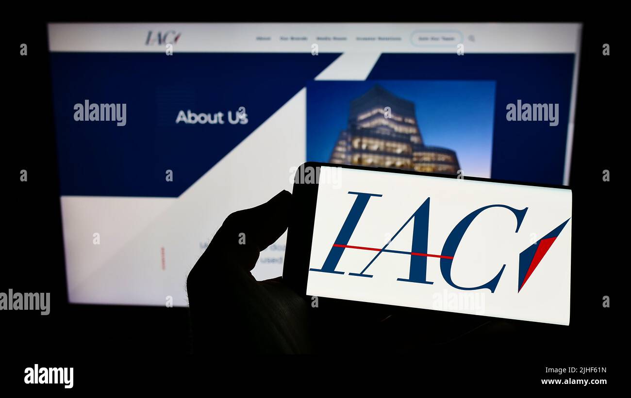 Person, die ein Mobiltelefon mit dem Logo des amerikanischen Medienunternehmens IAC InterActiveCorp auf dem Bildschirm vor der Webseite hält. Konzentrieren Sie sich auf die Telefonanzeige. Stockfoto