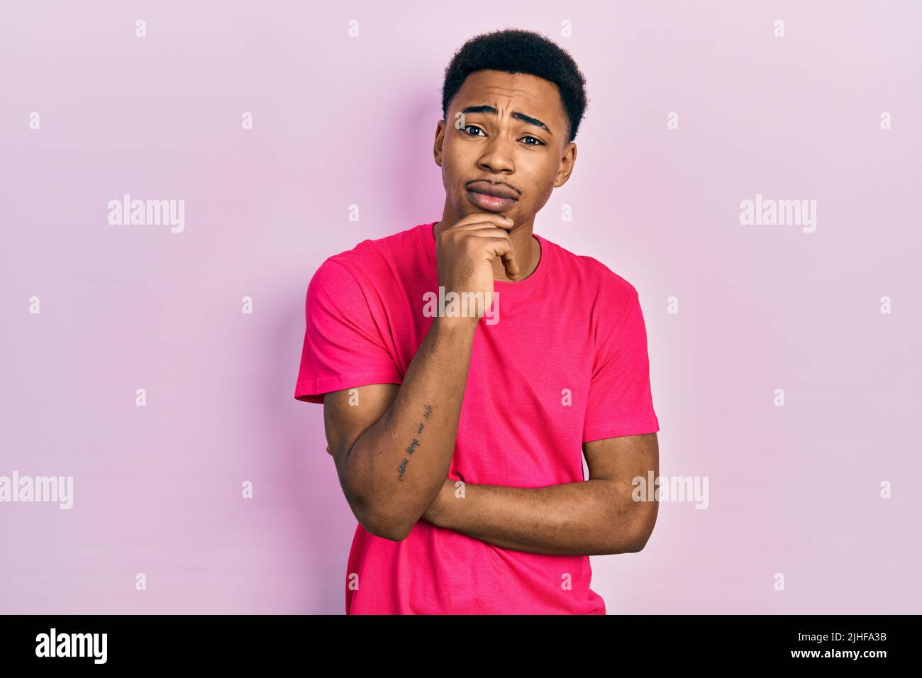 Junger afroamerikanischer Mann trägt Casua T-Shirt mit der Hand auf dem Kinn denken über Frage, nachdenklichen Ausdruck. Lächeln mit nachdenklichen Gesicht. Zweifel Co Stockfoto