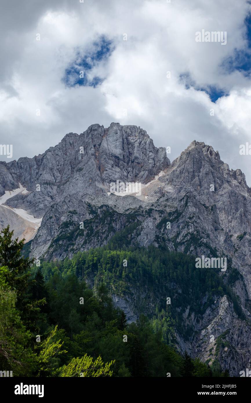 Die Gipfel liegen in der Sonne. Der Himmel ist bedeckt, aber zeigt blauen Himmel. Stockfoto