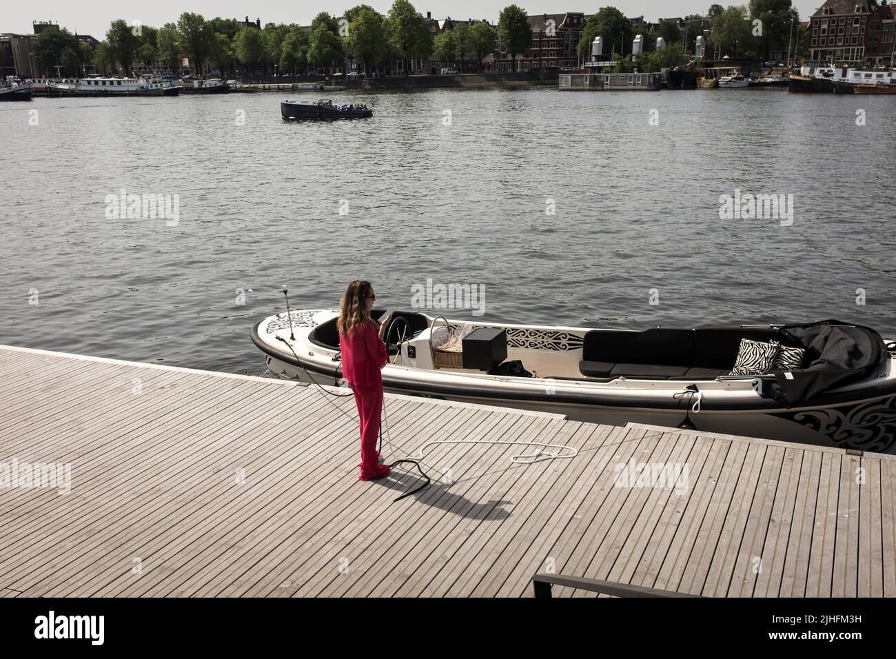 Eine erhöhte Ansicht einer Frau, die an einem heißen und sonnigen Tag in Amsterdam, Niederlande, die Anlegestelle eines Motorbootes an einem Kanal hält. Stockfoto