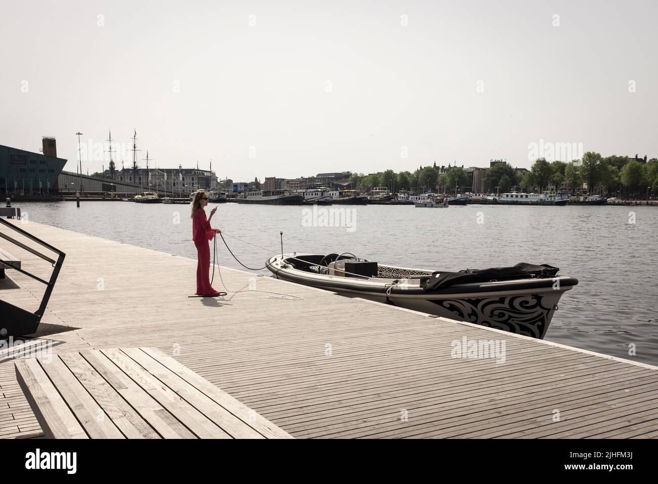 Eine Frau überprüft ihr Telefon, während sie an einem heißen und sonnigen Tag in Amsterdam, Niederlande, die Anlegestelle eines Motorbootes an einem Kanal hält. Stockfoto