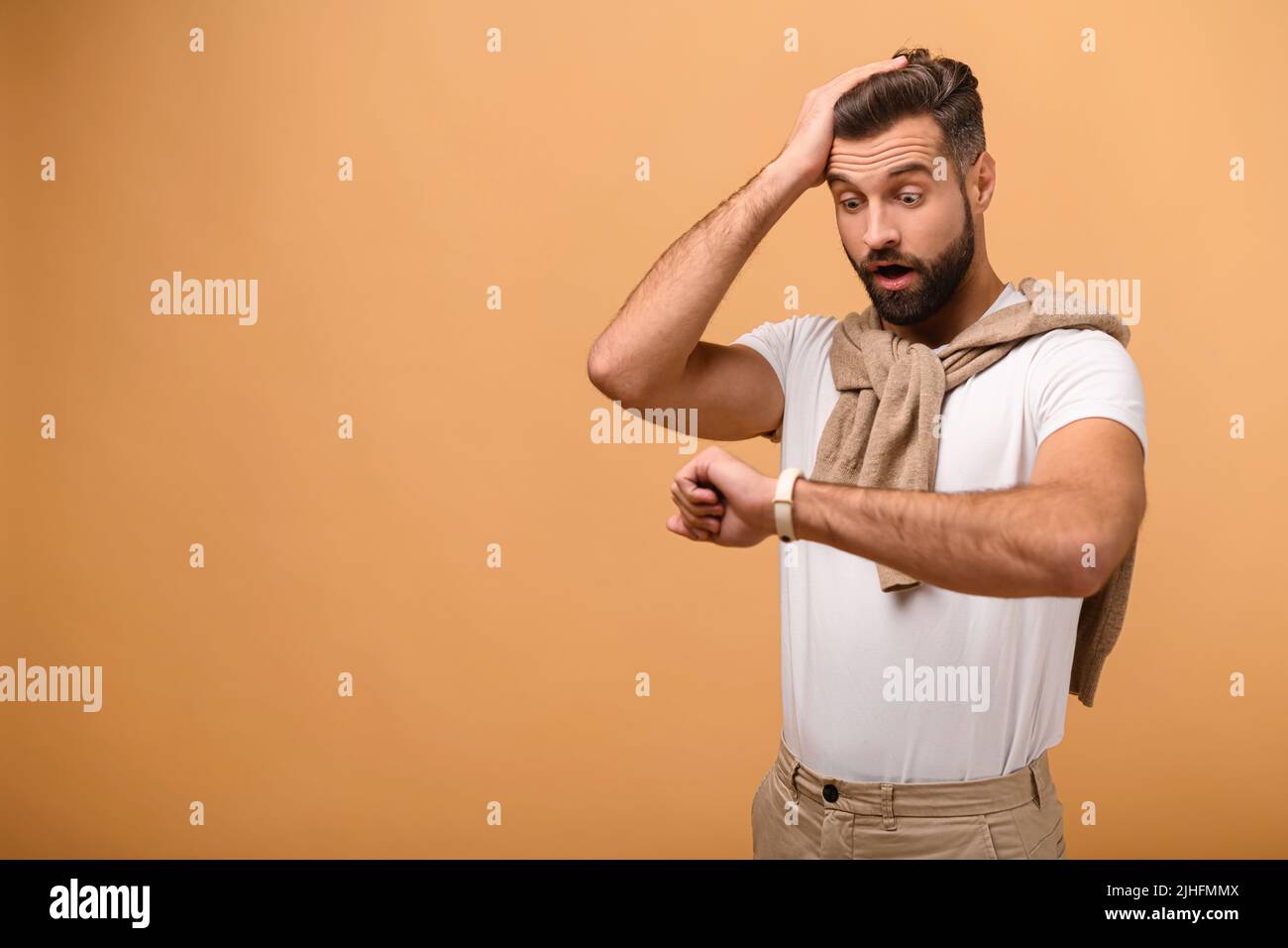 Ein junger, gutaussehender Geschäftsmann, der besorgt auf die Uhr schaute, Angst davor, zu spät zu kommen, isoliert auf orangefarbenem Hintergrund stand, vergaß das Treffen Stockfoto