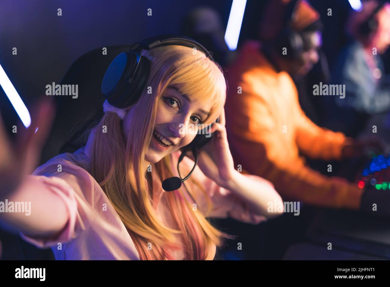 Blonde kaukasische hübsche Frau mit 20s Jahren, einem Headset und einem Mikrofon, die während eines Online-Spielturniers ein Selfie macht und in einem professionellen Spielzimmer sitzt. Hochwertige Fotos Stockfoto