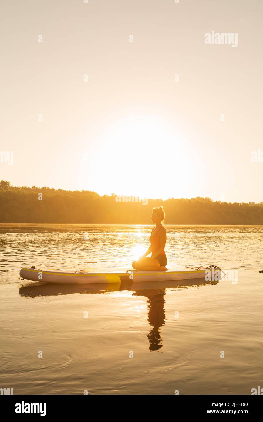 Eine Frau, die an einem heißen Sommertag auf einem Stand Up Paddle Board meditiert Stockfoto