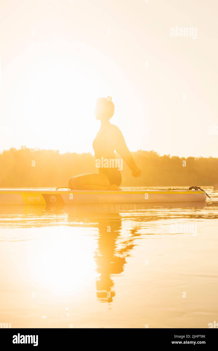 Silhouette einer Frau, die ihre Schultern streckt und sich auf Yoga vorbereitet, um sich während einer sommerlichen Hitzewelle abzukühlen Stockfoto
