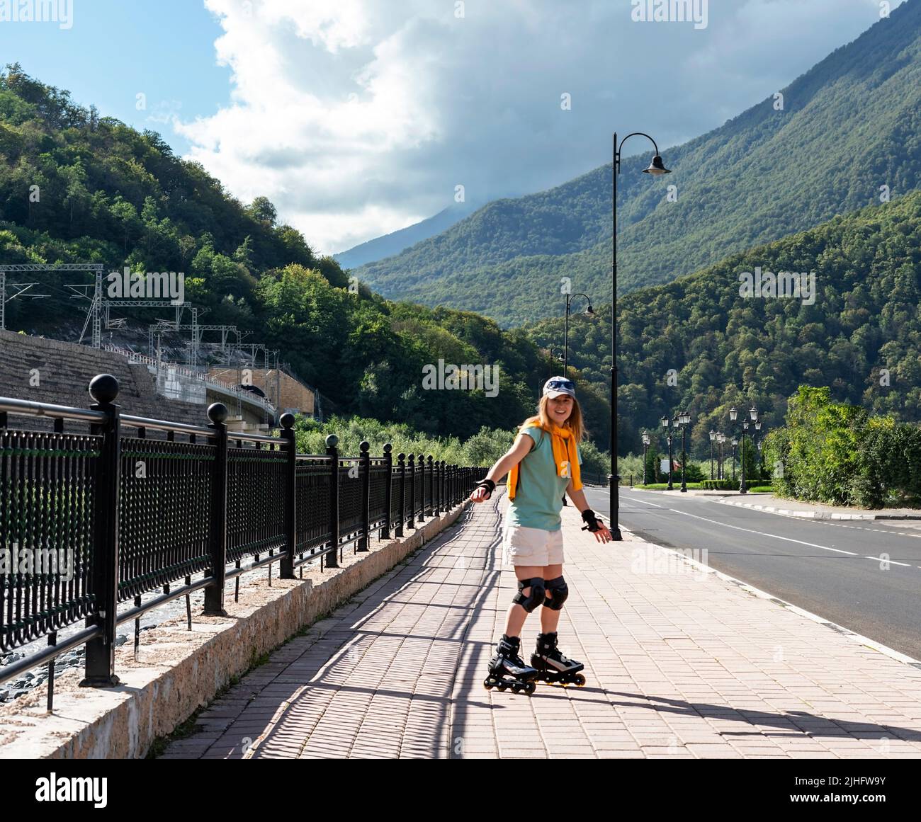 Glückliche junge Frau in Schutzausrüstung Reiten auf Rollschuhe entlang Böschung im Sommer aktiven Lebensstil, Outdoor-Aktivitäten, Rollschuhlaufen Stockfoto
