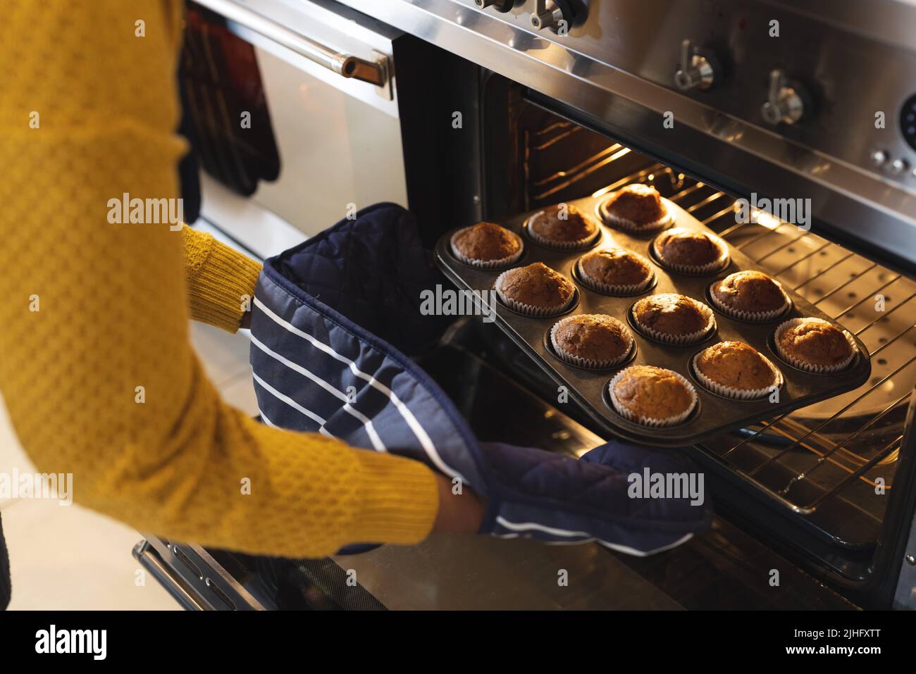 Bild des mittleren Abschnitts einer afroamerikanischen älteren Frau, die Cupcakes aus dem Ofen herausnahm Stockfoto