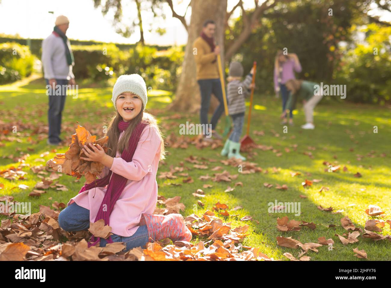 Bild eines glücklichen kaukasischen Mädchens, das im Garten mit Herbstblättern spielt Stockfoto