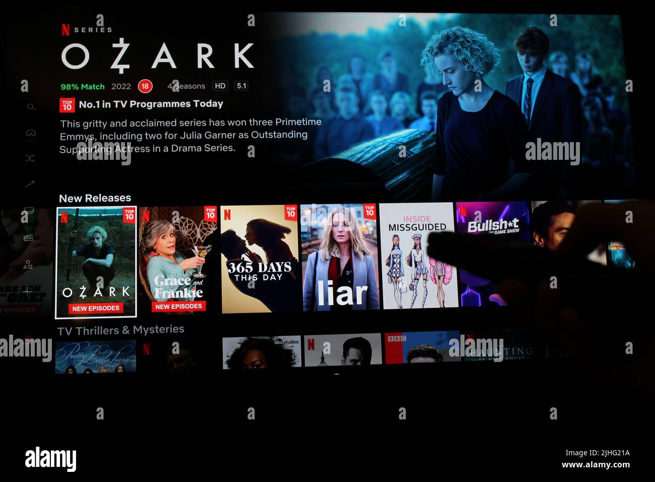 London, Großbritannien: 1. Mai 2022: Netflix-App auf dem fernsehbildschirm, die die Show Ozark mit dem Schatten einer Person zeigt, die eine TV-Fernbedienung vor sich hält. Stockfoto