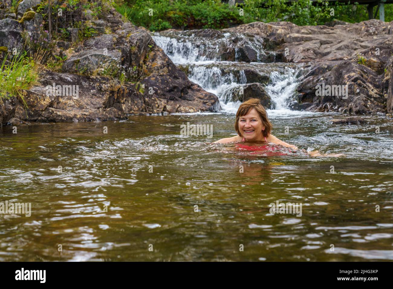 Frau, die in einem Wasserbecken im Storforsen-Naturschutzgebiet, Kreis Älvsbyn, Provinz Norrbotten, Schweden schwimmt Stockfoto