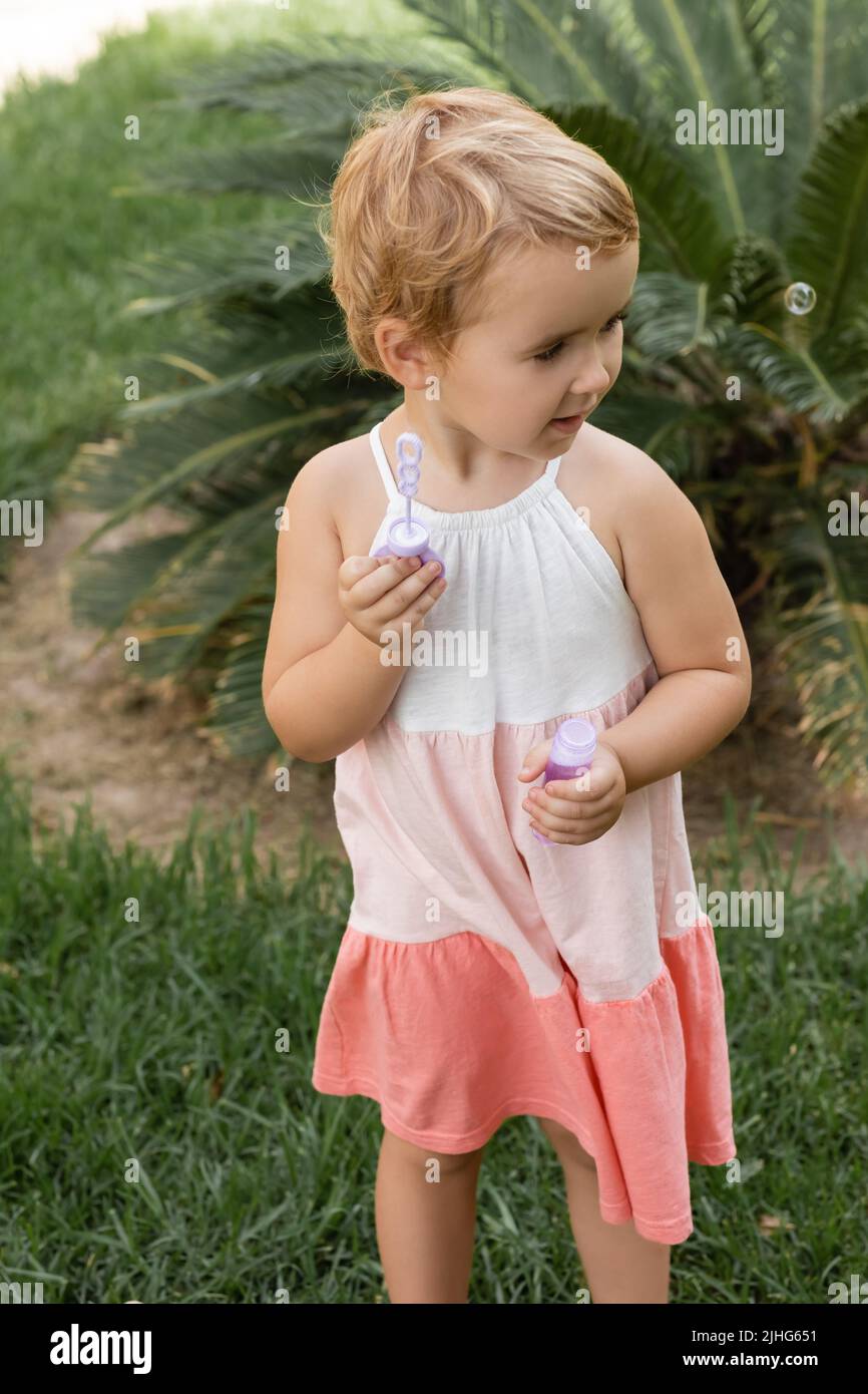 Kleinkind Kind im Sommerkleid hält Seifenblasen auf dem Rasen Stockfoto
