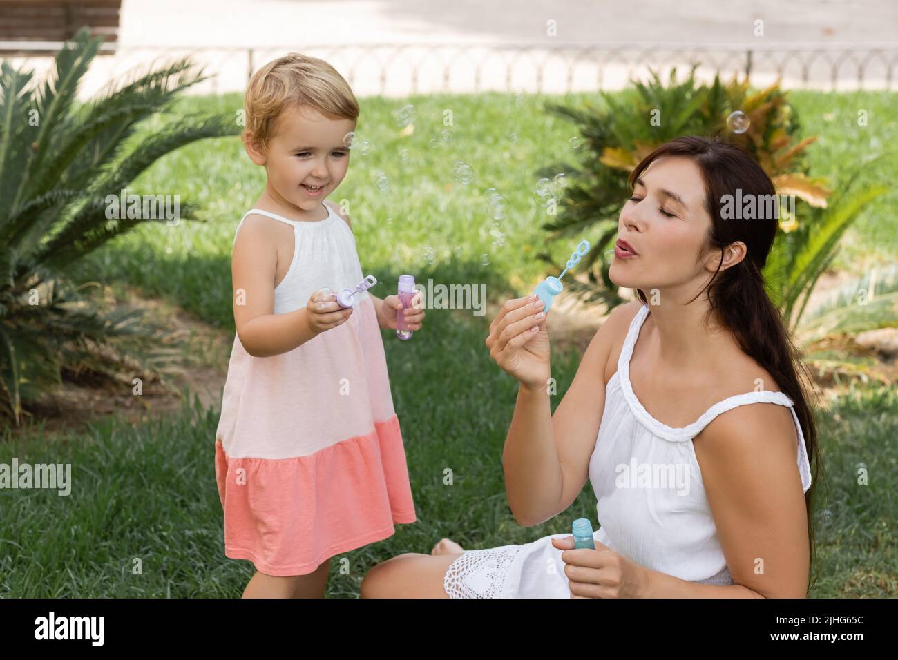 Positives Kind hält Seifenblasen in der Nähe der Mutter auf dem Rasen Stockfoto