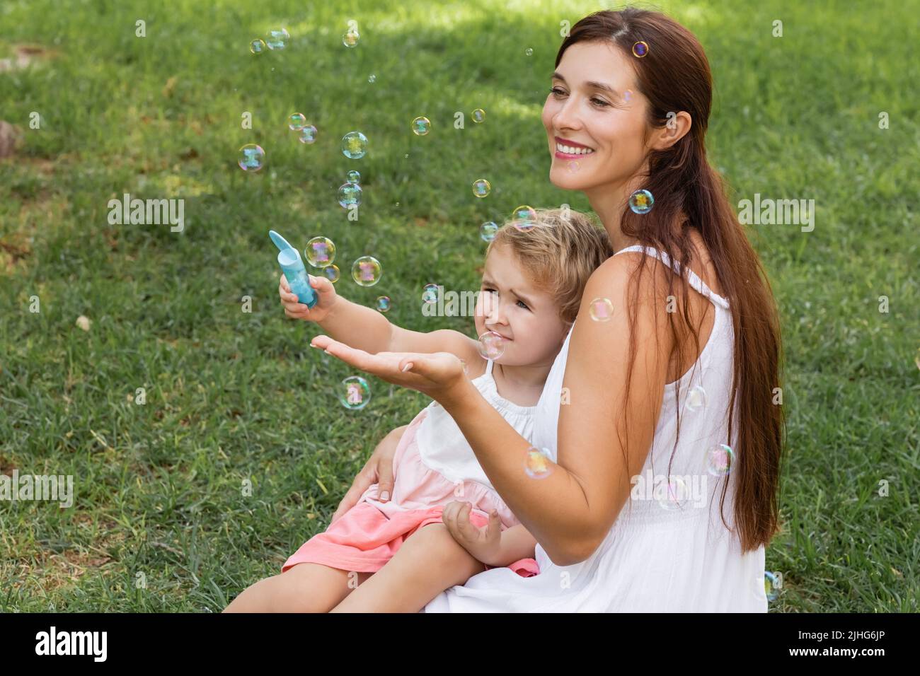 Positive Mutter und Kleinkind spielen mit Seifenblasen im Sommerpark Stockfoto