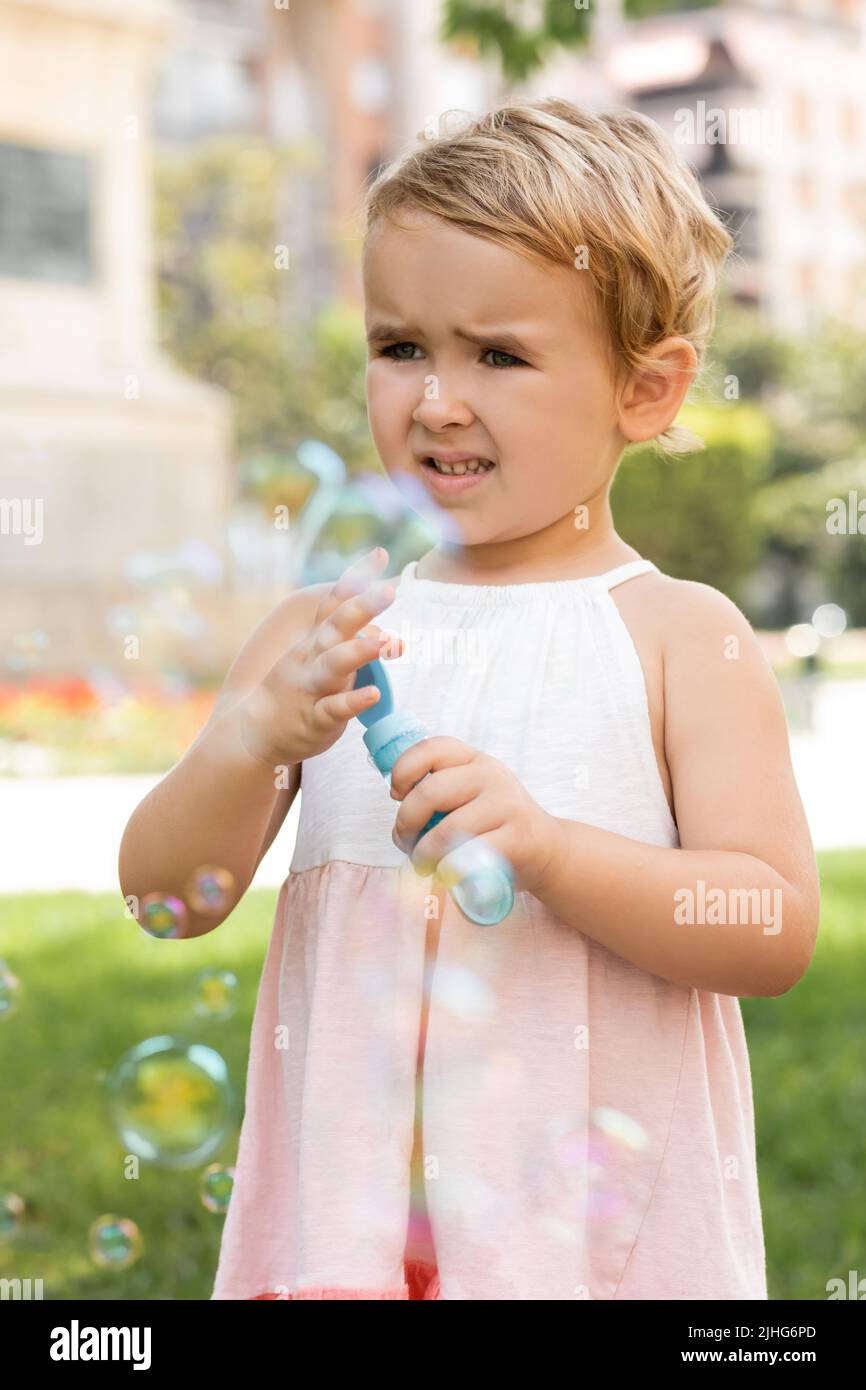 Portrait von fokussierten Baby Mädchen in Kleid hält Seifenblasen im Park Stockfoto