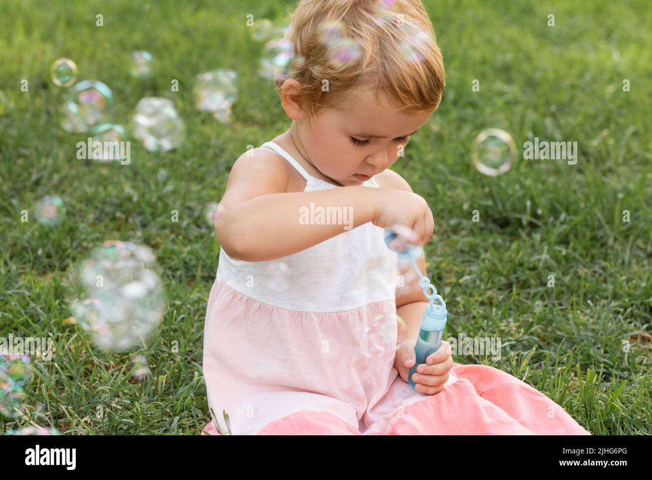 Fokussiertes Baby Mädchen hält Seifenblasen auf Gras im Park Stockfoto