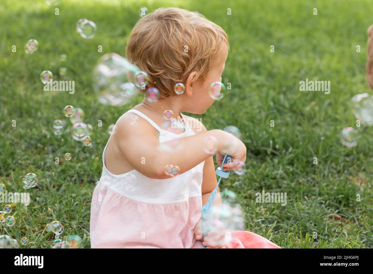 Seitenansicht von Baby-Mädchen in Kleid hält Seifenblasen im Sommer Park Stockfoto