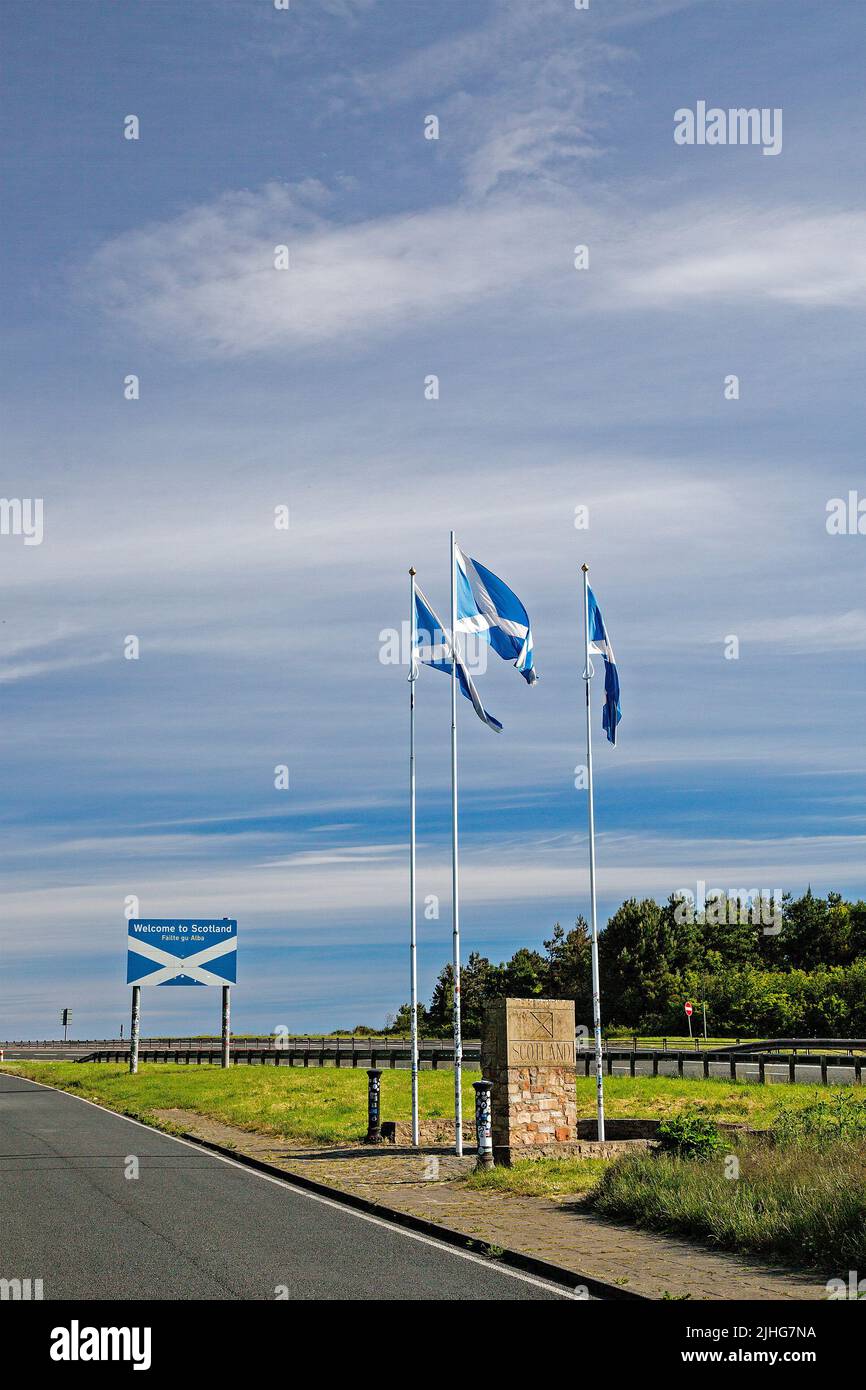 Die Grenze zwischen England und Schottland bei Berwick-upon-Tweed ist durch die schottischen Flaggen und einen Steinsockel gekennzeichnet. Ein strahlend blauer Himmel mit wispigen Wolken. Stockfoto