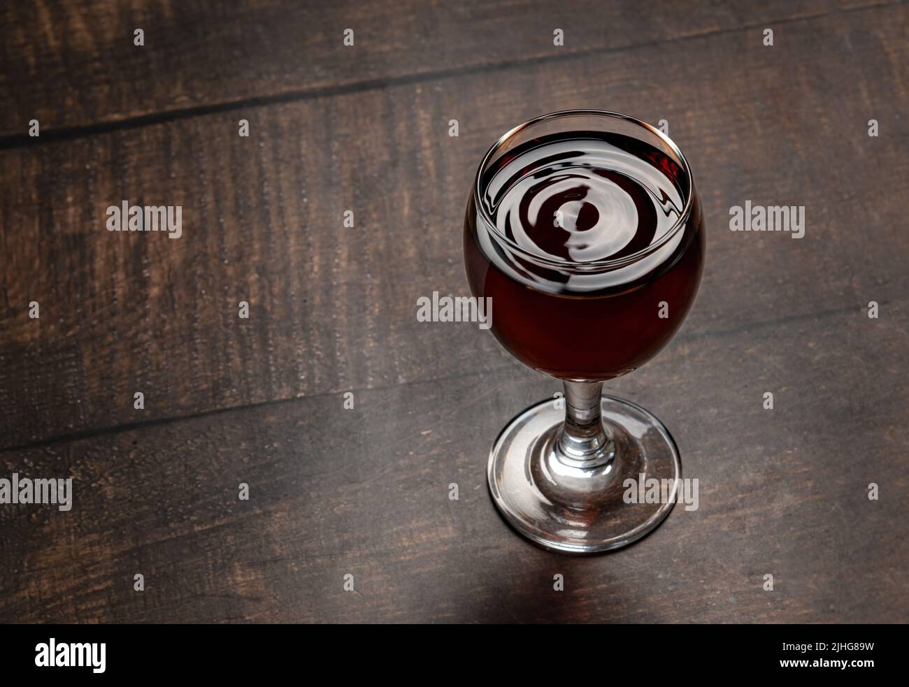 Tropfen Wein und Wellen bilden sich in einem Glas voller Rotwein, das auf einem Holztisch steht Stockfoto