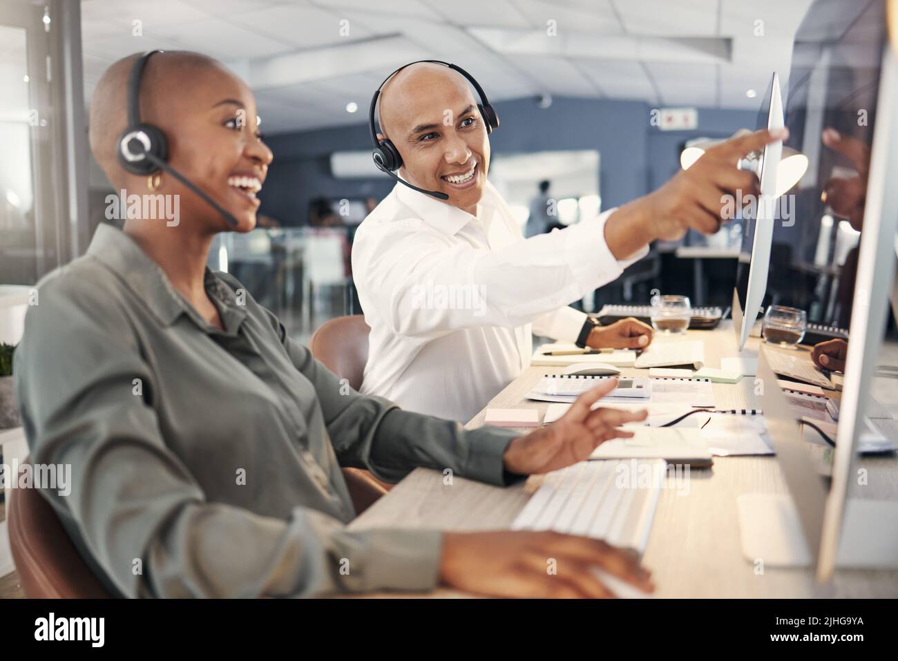 Gemischter, männlicher Callcenter-Telemarketing-Agent diskutiert mit Kollegen Pläne, während er in einem Büro am Computer arbeitet. Zwei Berater Stockfoto