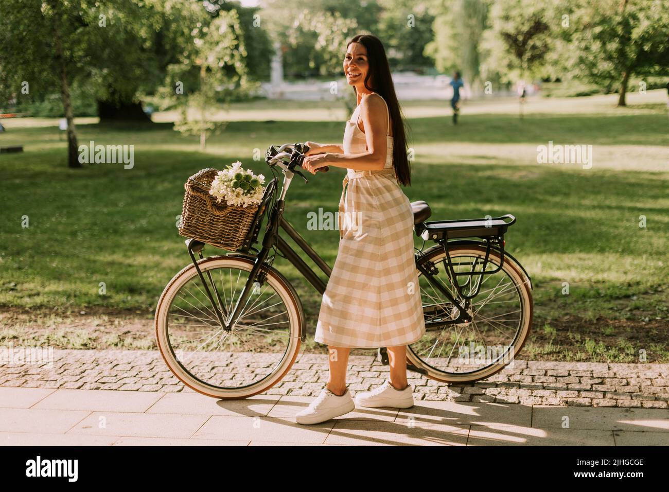 Hübsche junge Frau mit Blumen im Korb des Elektrofahrrads Stockfoto