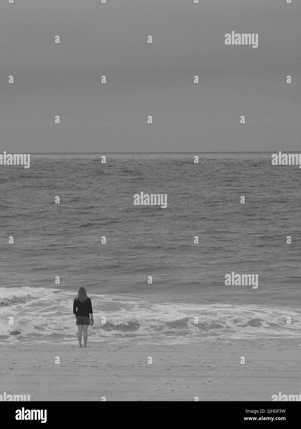 Eine einsame Frau am Strand hielt morgens ein Glas in der Hand, während sie auf das Meer starrte. Stockfoto