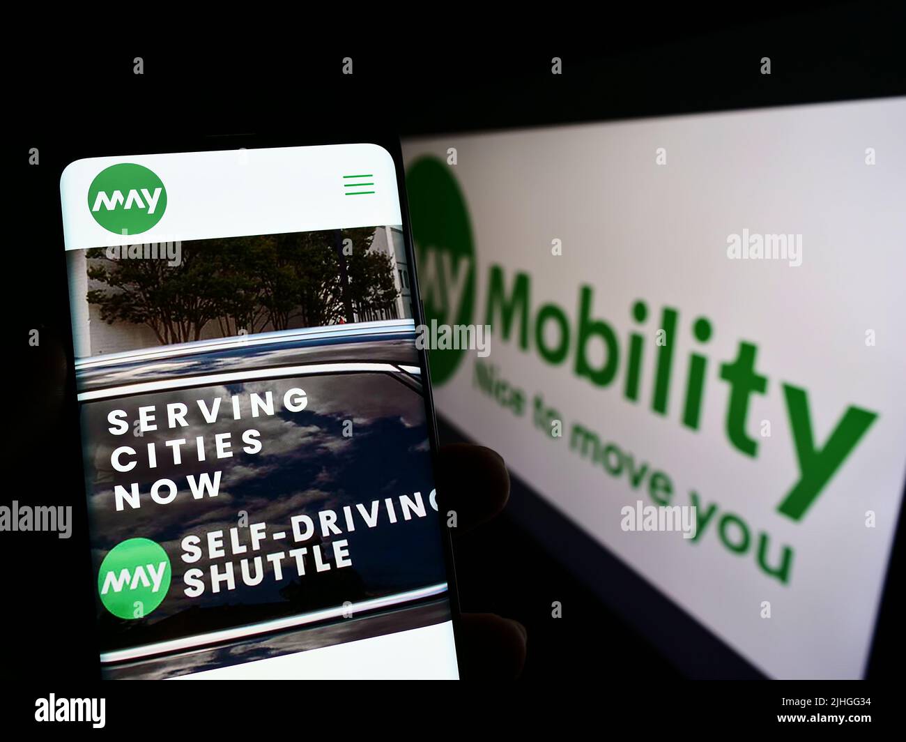 Person, die Mobiltelefon mit der Webseite des US-Selbstfahrers May Mobility Inc. Auf dem Bildschirm vor dem Logo hält. Konzentrieren Sie sich auf die Mitte des Telefondisplays. Stockfoto