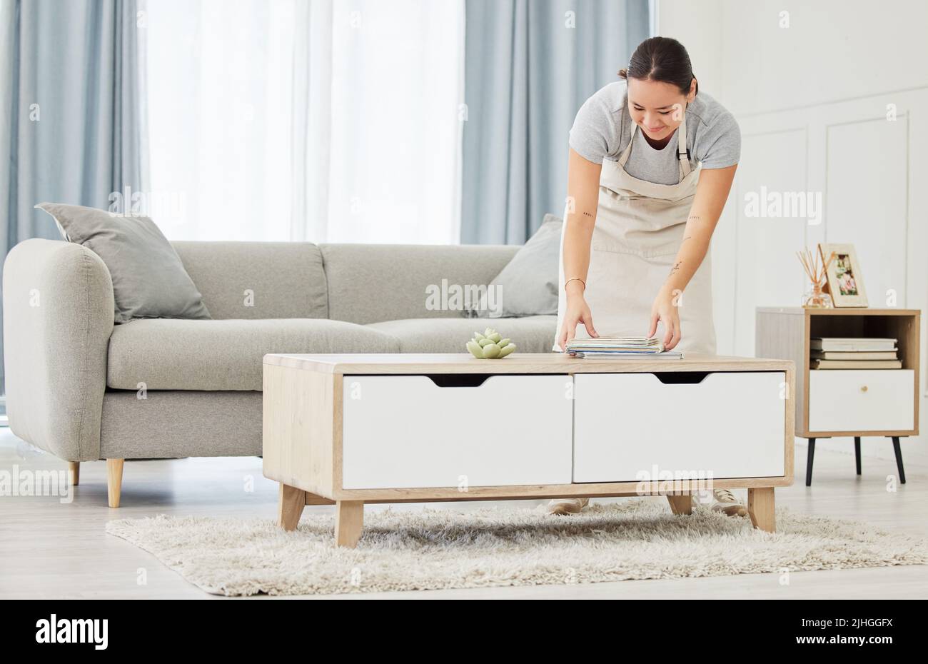 Eine schöne lächelnde junge Frau mit gemischter Rasse, die die Oberflächen ihres Hauses putzt. Glückliche asiatische Hausangestellte Verpackung Bücher in einen ordentlichen Haufen auf die Stockfoto