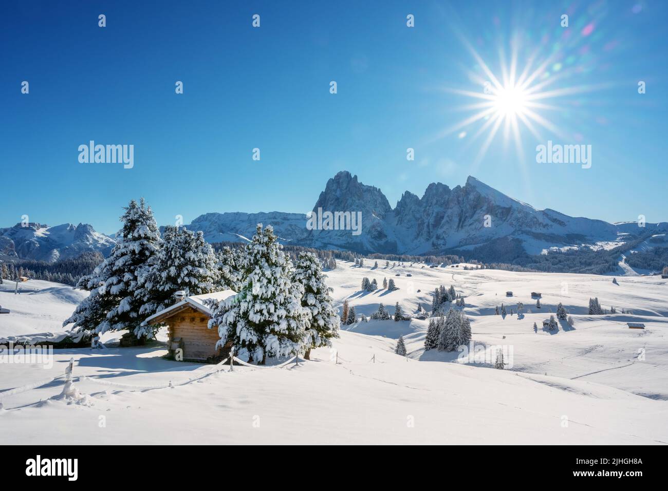 Malerische Landschaft mit kleiner Holzhütte auf der Seiser Alm bei Sonnenaufgang. Seiser Alm, Dolomiten, Italien. Verschneite Hügel mit orangefarbener Lärche und Langkofelgruppe Stockfoto