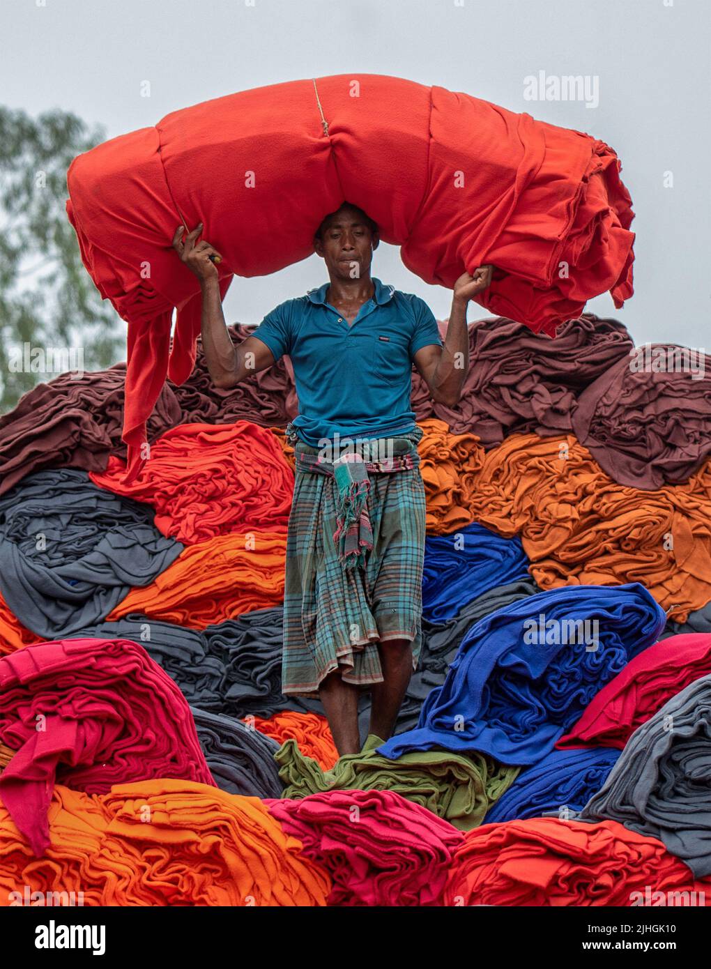 Bunte Decken werden von Arbeitern auf LKWs geladen. Textilindustrie in Bangladesch Stockfoto