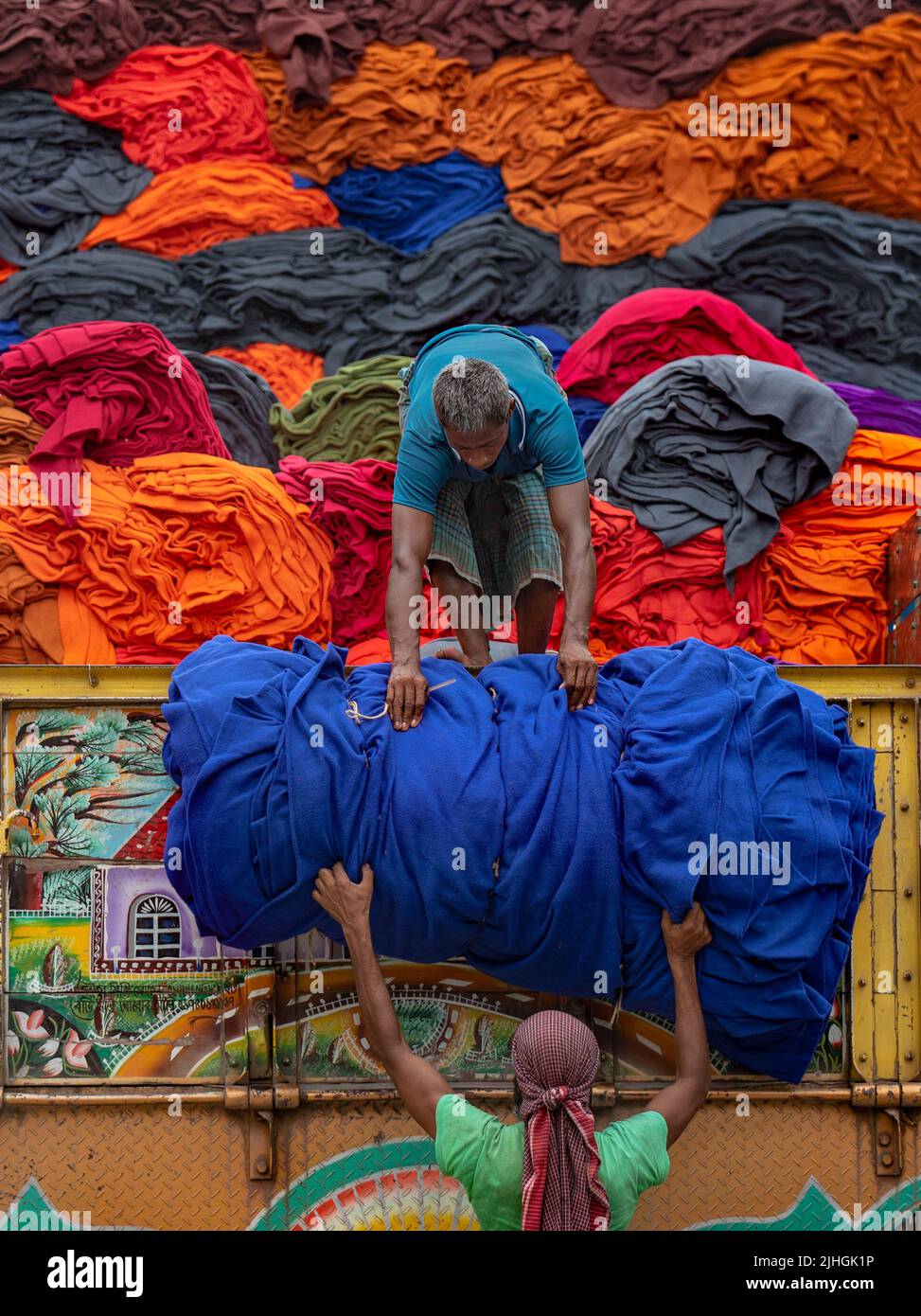 Bunte Decken werden von Arbeitern auf LKWs geladen. Textilindustrie in Bangladesch Stockfoto