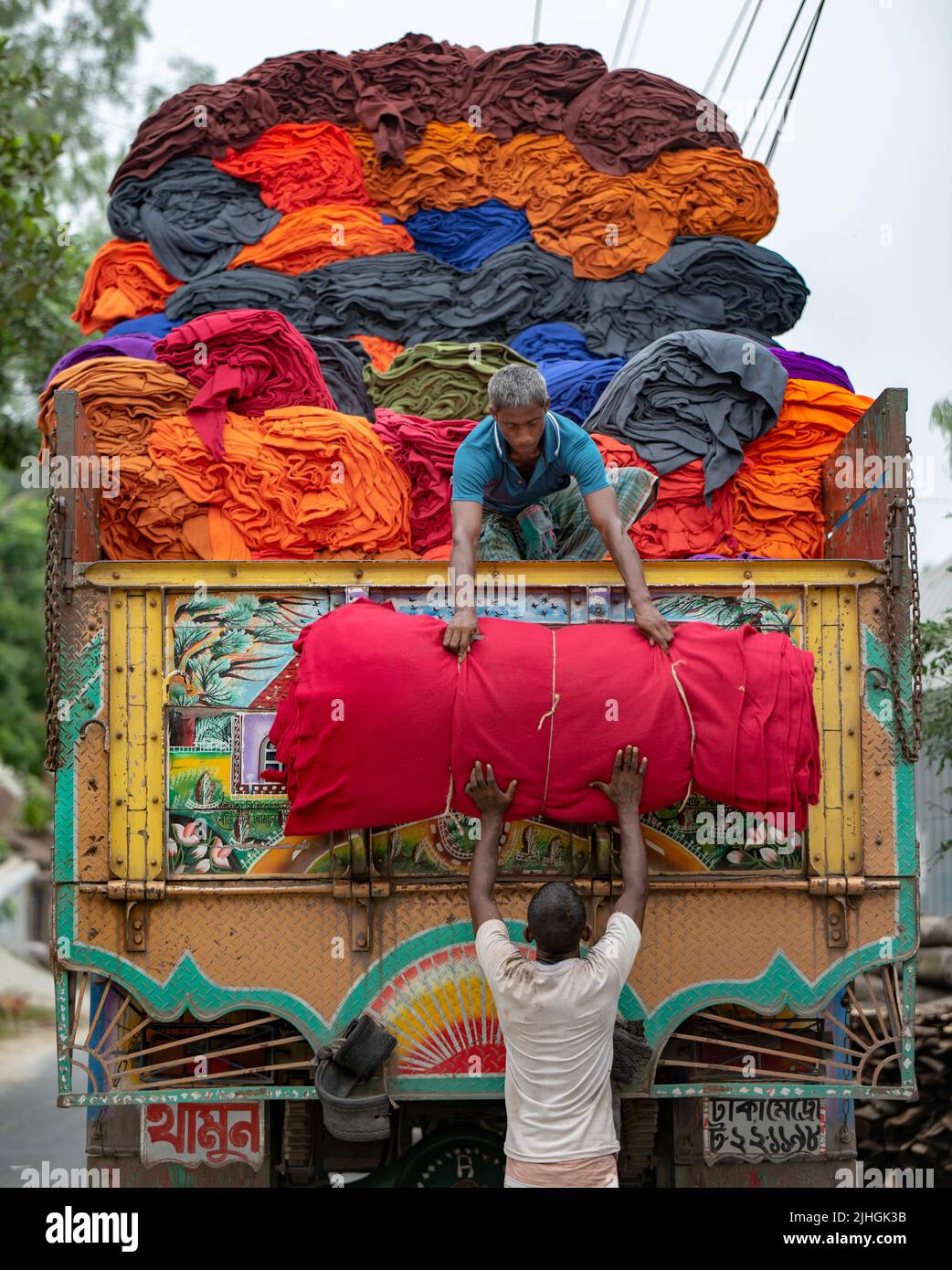 Bunte Decken werden von Arbeitern auf LKWs geladen. Textilindustrie in Bangladesch Stockfoto