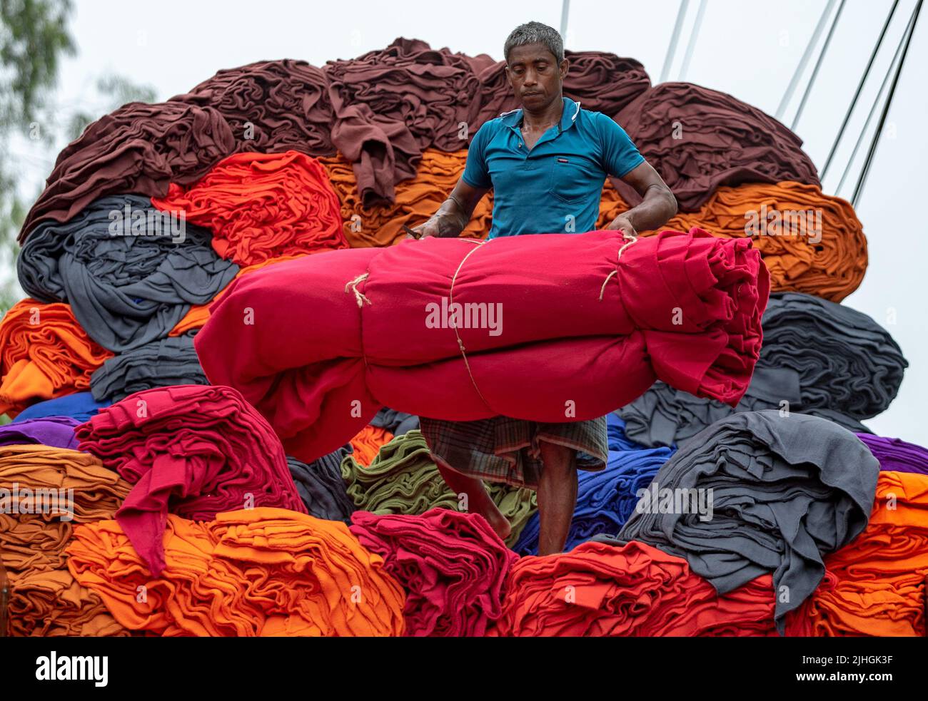 Bunte Decken werden von Arbeitern auf LKWs geladen. Textilindustrie in Bangladesch Stockfoto