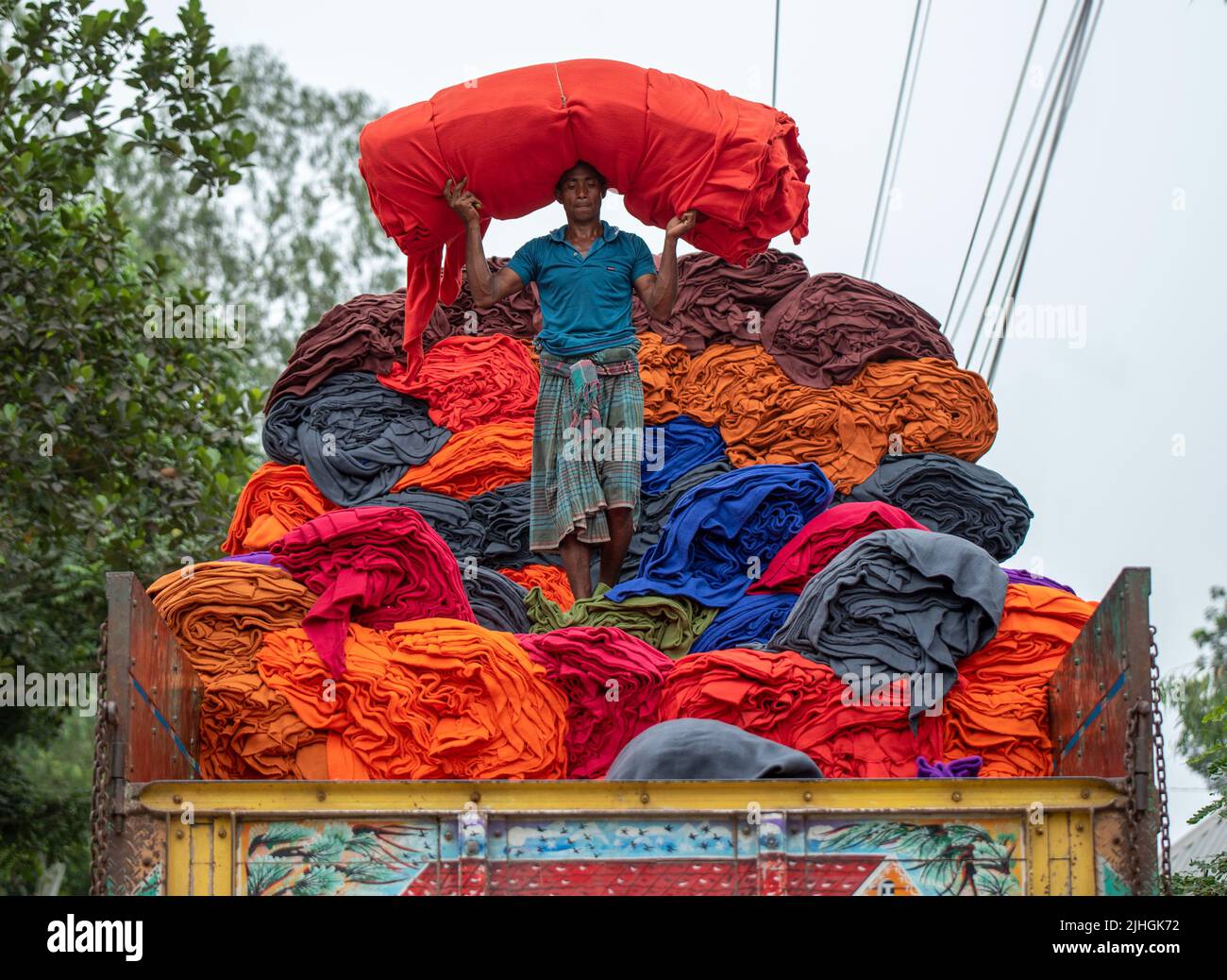 Bunte Decken werden von Arbeitern auf LKWs geladen. Textilindustrie in Bangladesch Stockfoto