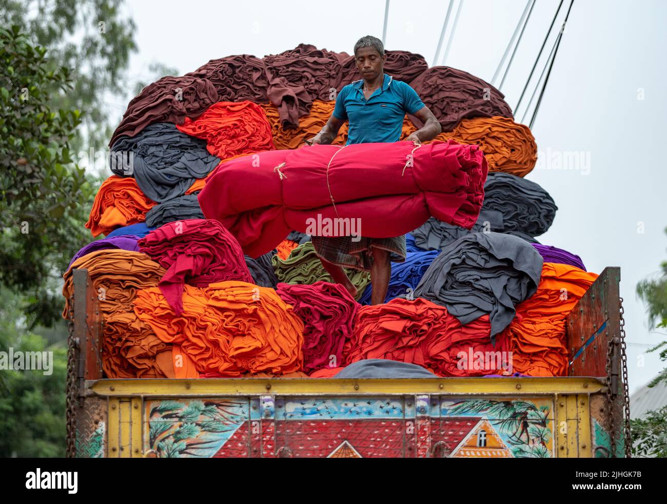 Bunte Decken werden von Arbeitern auf LKWs geladen. Textilindustrie in Bangladesch Stockfoto