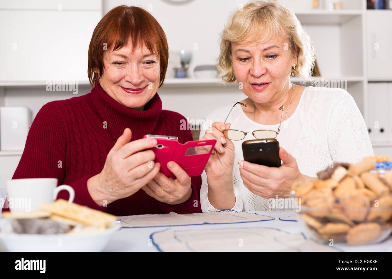 Zwei positive ältere Frauen, die Telefone benutzen Stockfoto