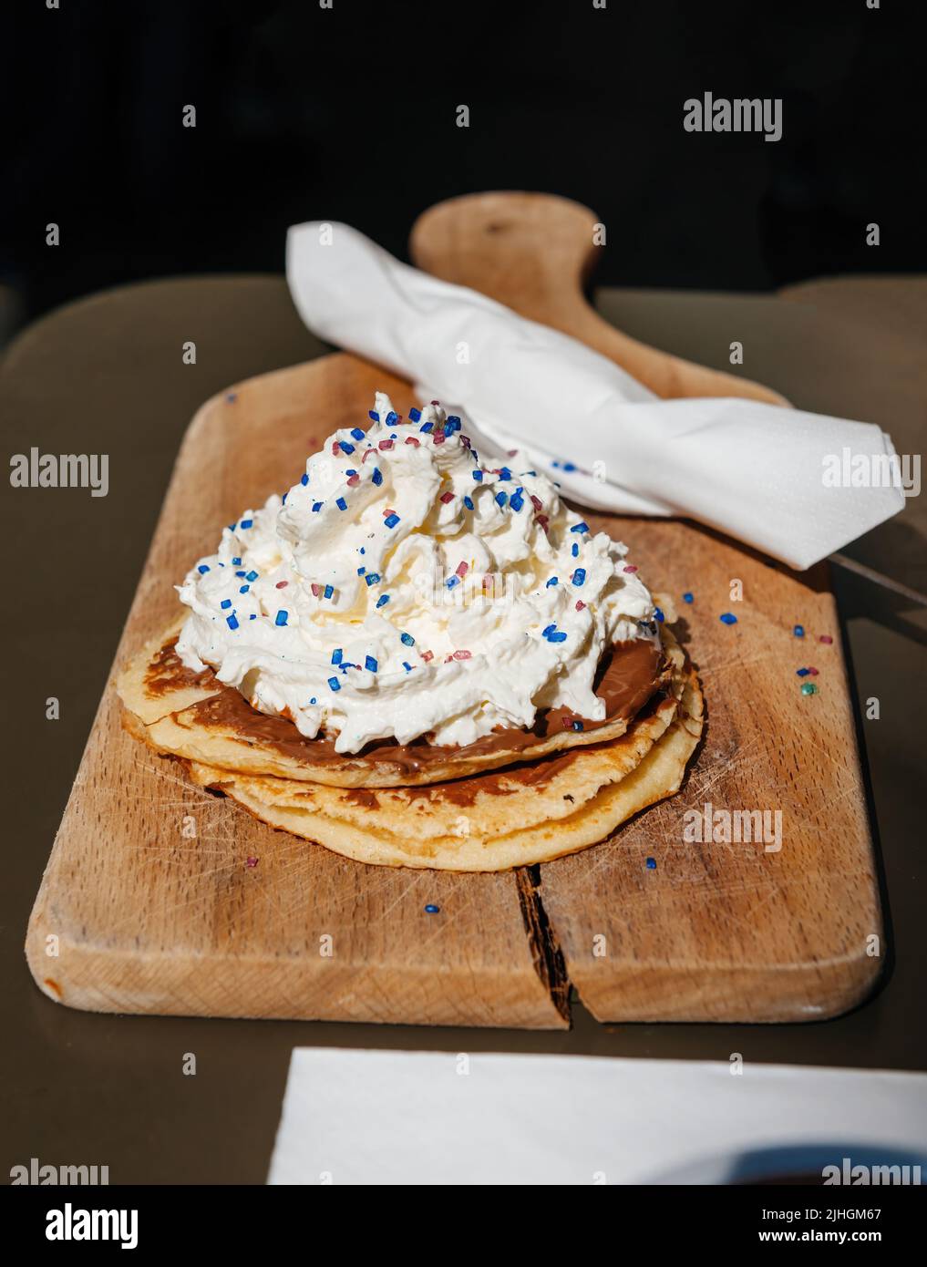 Nahaufnahme von leckeren Pfannkuchen, serviert auf Holzplatte mit köstlicher Creme und bunten Mini-Bonbons in französischer Bäckerei Stockfoto