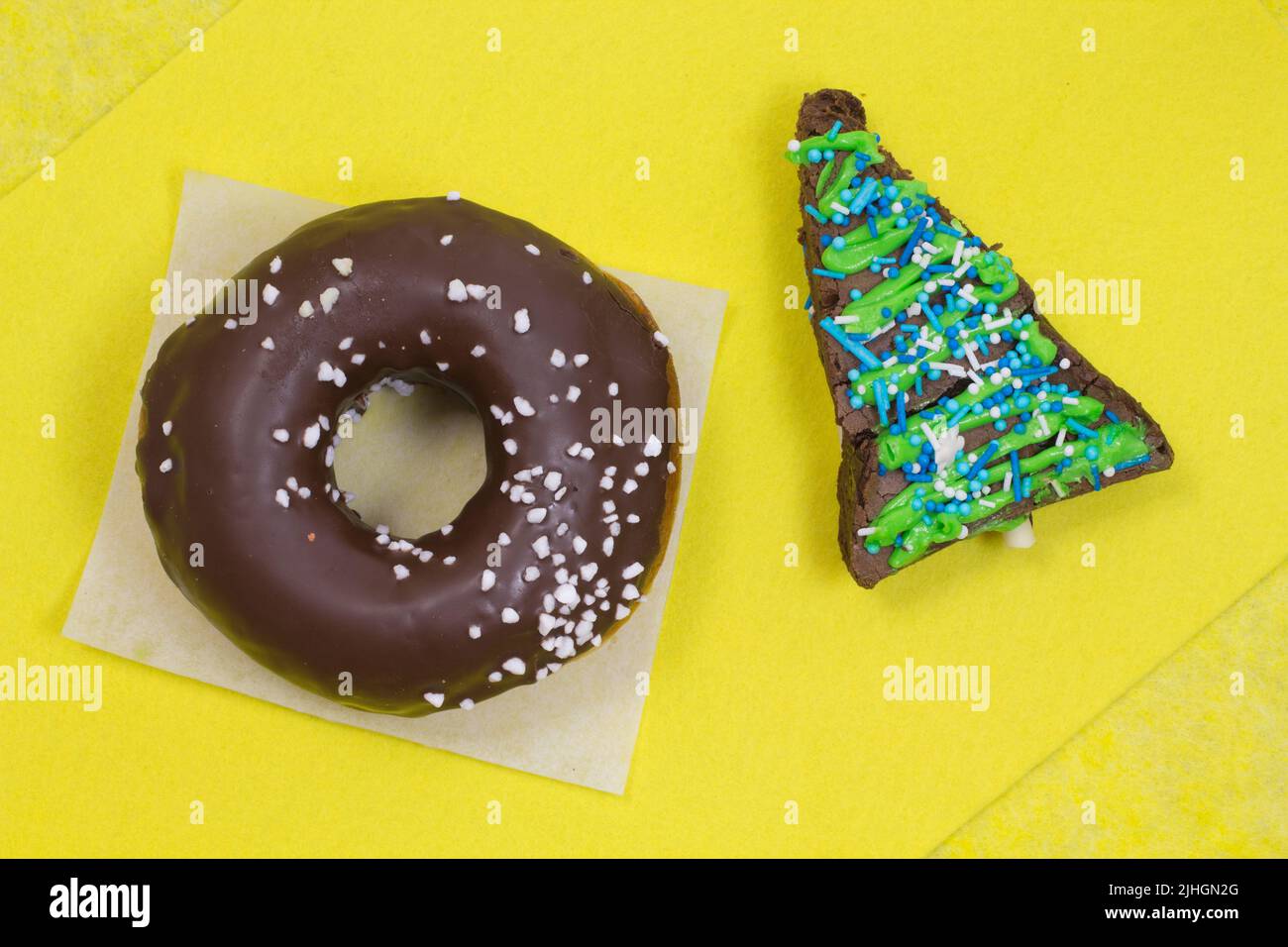 Brownie-Kuchen in Form eines Dreiecks und braun glasierten Donut auf gelbem Hintergrund Stockfoto