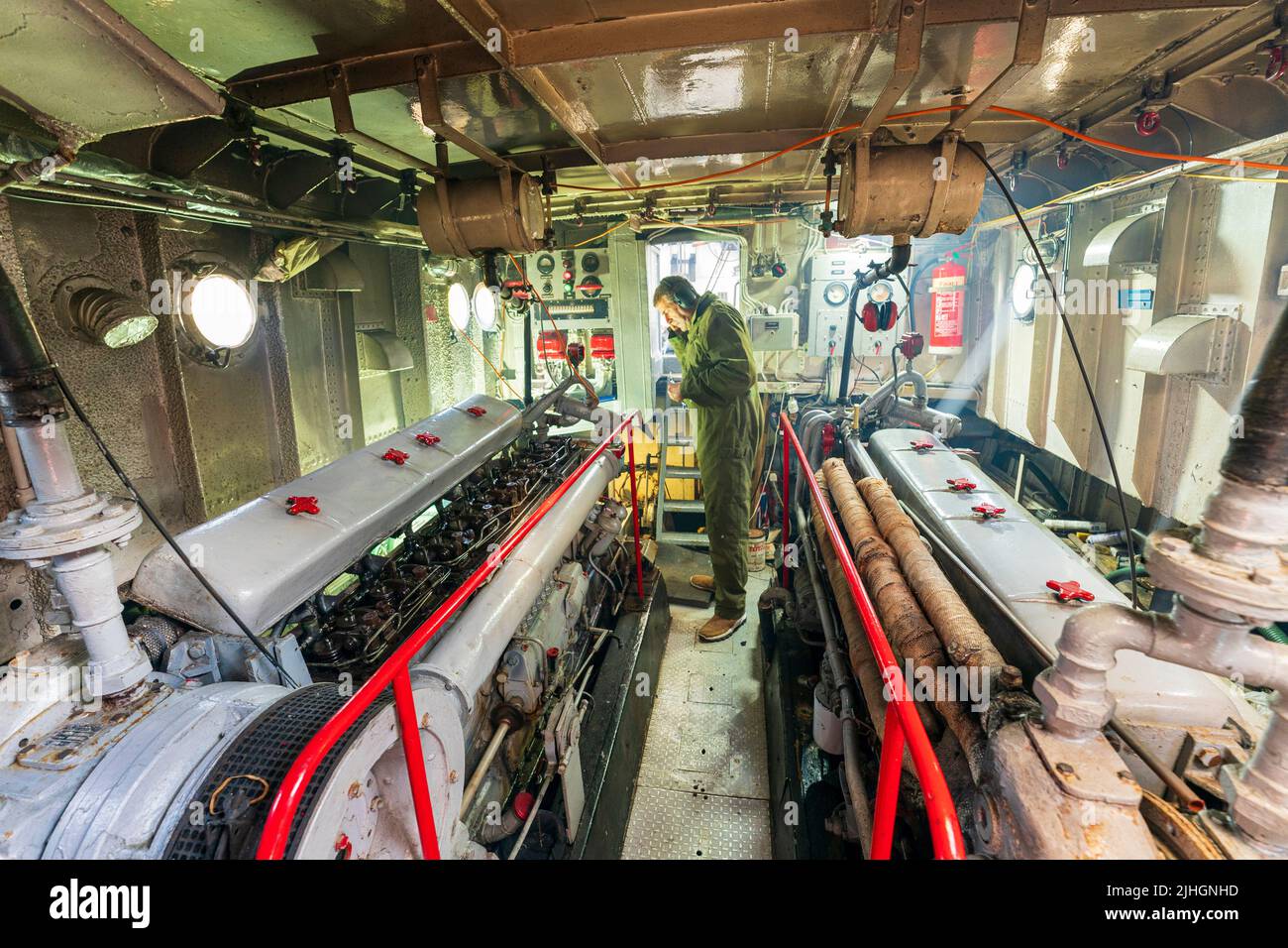 Mann, Ingenieur, stehend zwischen zwei großen Dieselmotoren, einer mit offener Abdeckung, im Maschinenraum des Rheinschiffs der US Navy aus den 1950er Jahren, P22 Stockfoto