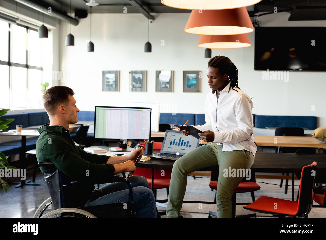 Der junge afroamerikanische Geschäftsmann diskutiert mit einem kaukasischen Kollegen, der im Rollstuhl sitzt Stockfoto