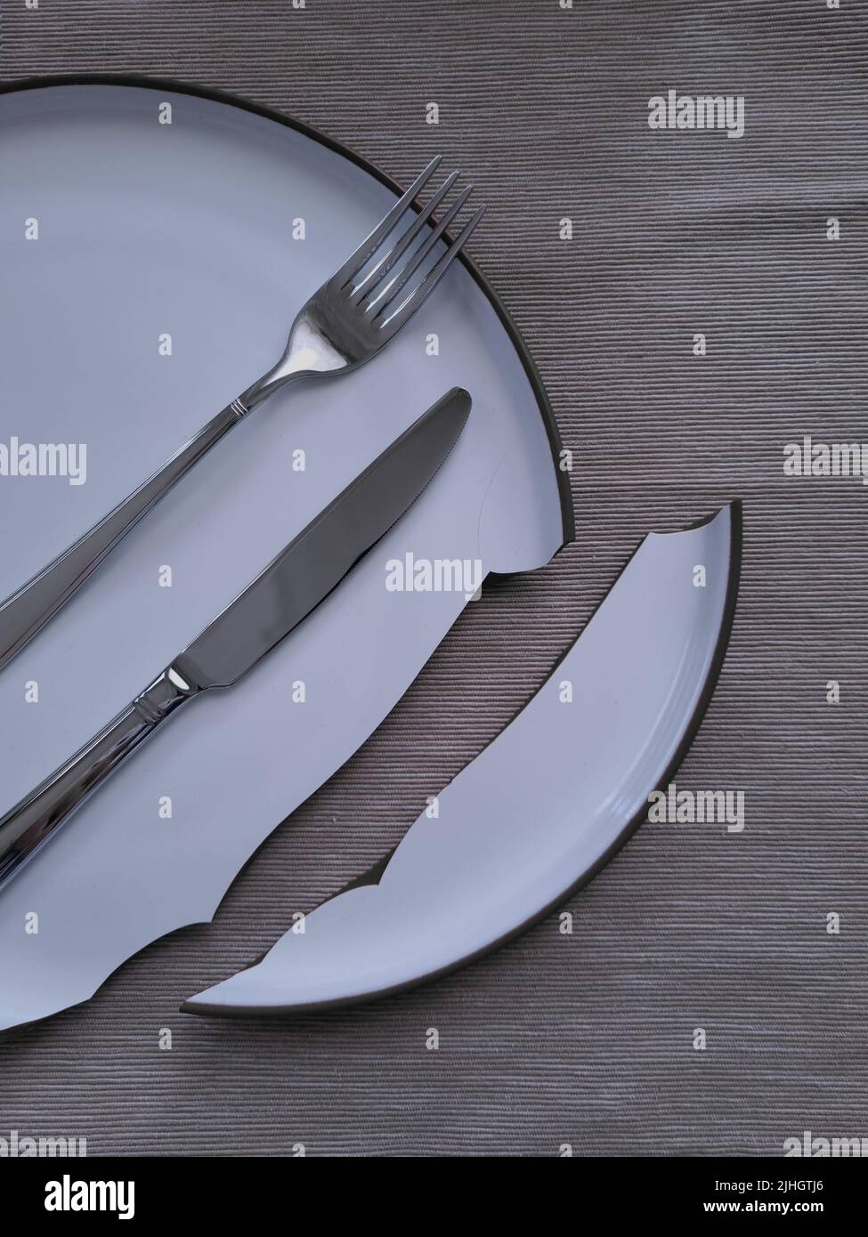 Geschirr über den zerbrochenen Teller legen. Messer und Gabel auf dem Speiseteller. Unglück in der Küche. Stockfoto