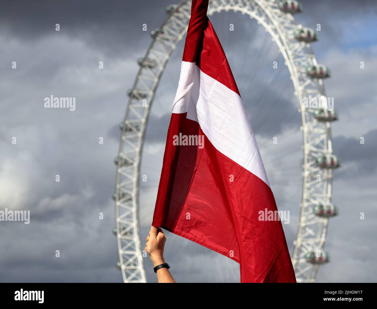 London, Großbritannien - 23. August 2020: Lettische Flagge mit London Eye und bewölktem Himmel im Hintergrund Stockfoto