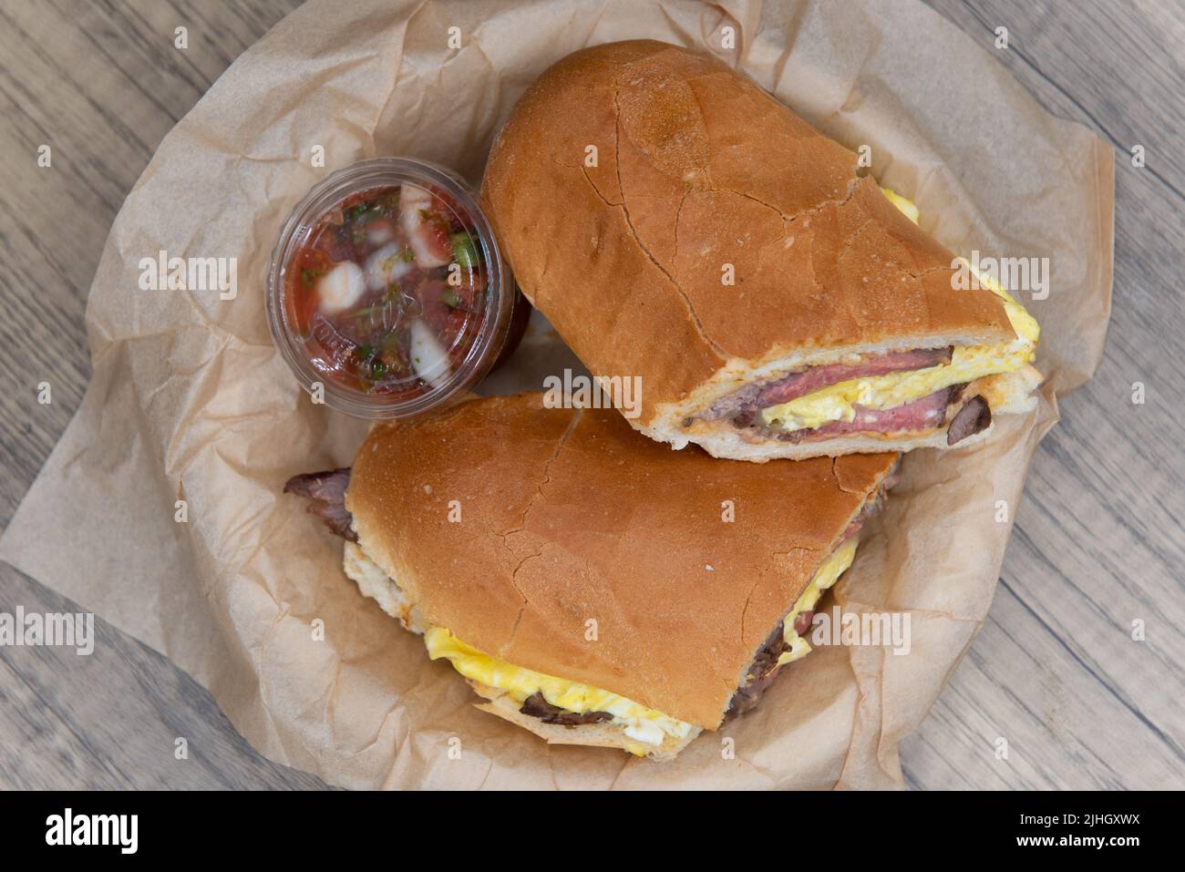 Blick von oben auf das Frühstücksteak und das Rühreier-Sandwich, das mit Eiweiß beladen und in eine italienische Rolle eingewickelt war. Stockfoto