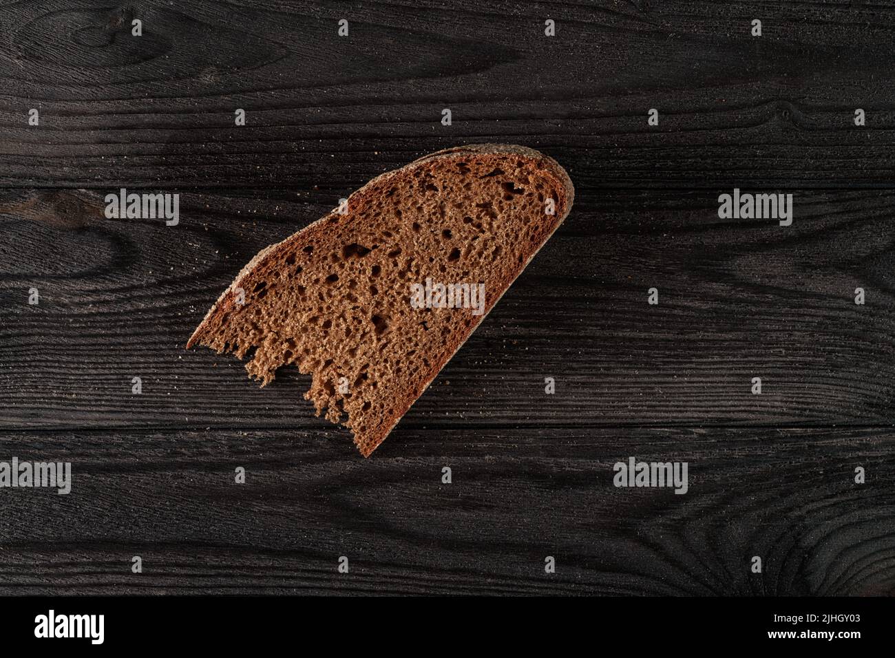 Braunes kleines Stück Brot auf schwarzem Holztisch. Dunkles HDR-Foto. Einfache Lebensmittel, magere Lebensmittel, Armut und Unterernährung Stockfoto