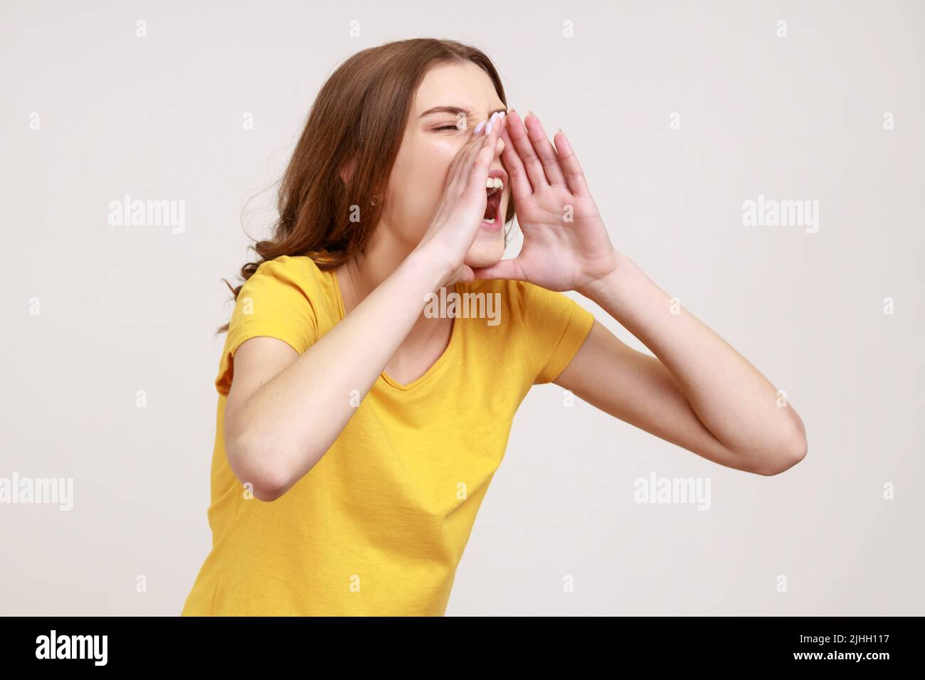 Das Profil eines Teenagers im gelben T-Shirt hält die Arme weit offen, schreit laut, macht auf wichtige Nachrichten aufmerksam und kündigt das Ereignis an. Innenaufnahme des Studios isoliert auf grauem Hintergrund. Stockfoto