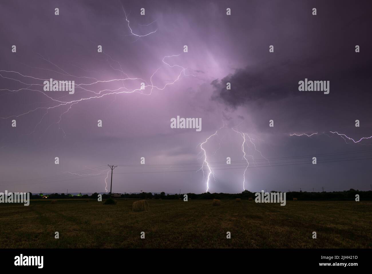Gewitter über dem Feld mit Heuballen in der Nacht, Wolken zu Boden verzweigten Blitzen, Blitz in Wolken in der Nacht in der Landschaft Stockfoto