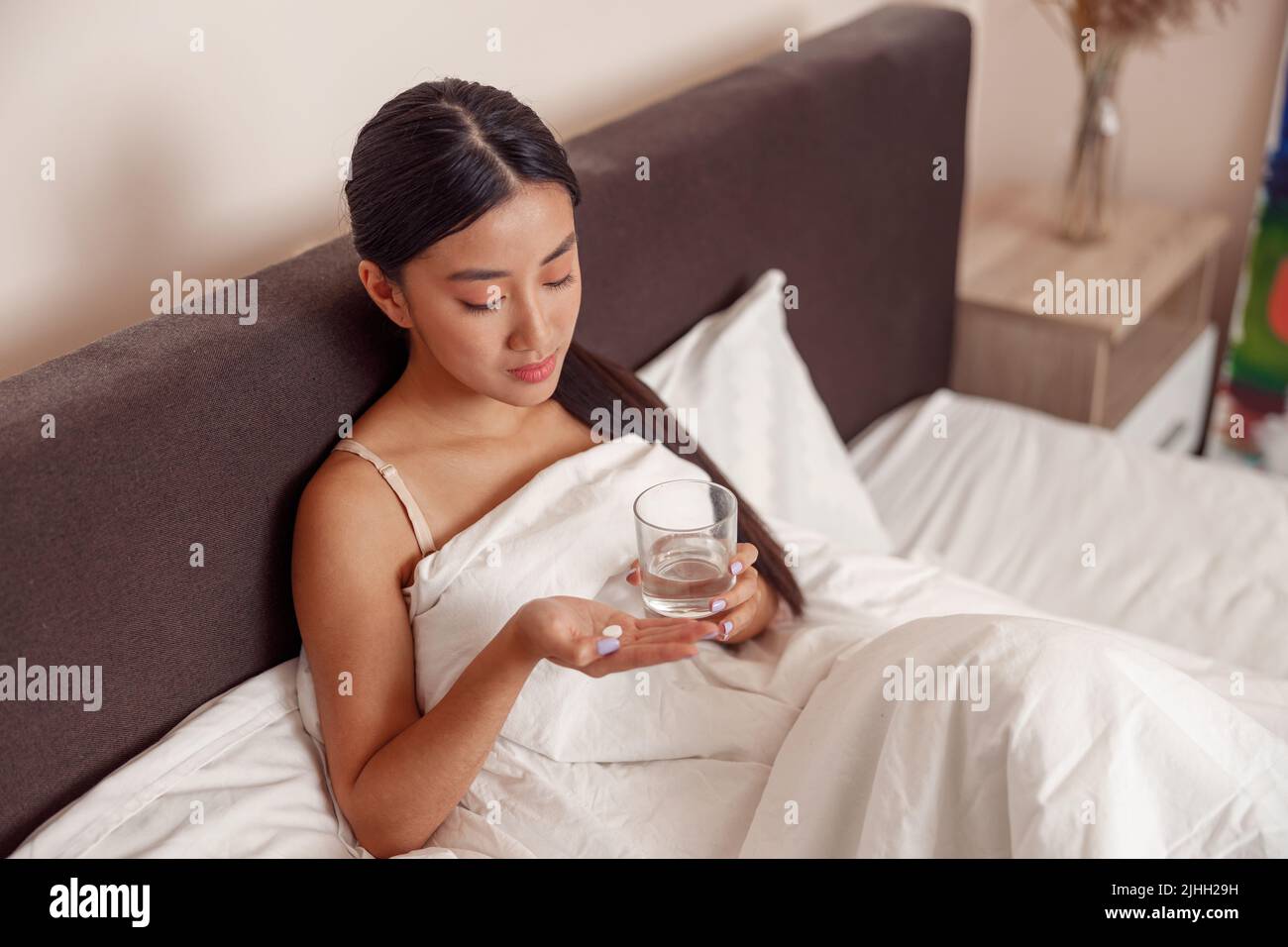 Asiatische junge Frau mit Pille in der Hand im Bett zu Hause liegen Stockfoto