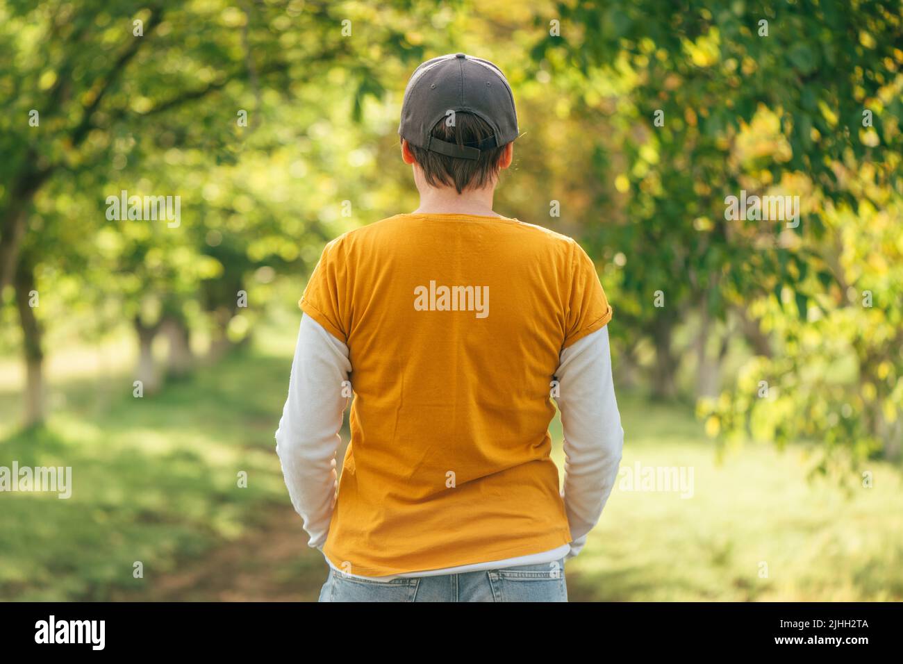 Rückansicht einer Farmerin mit orangefarbenem T-Shirt und Truckerhut in einem Obstgarten aus Nussbaum, selektiver Fokus Stockfoto