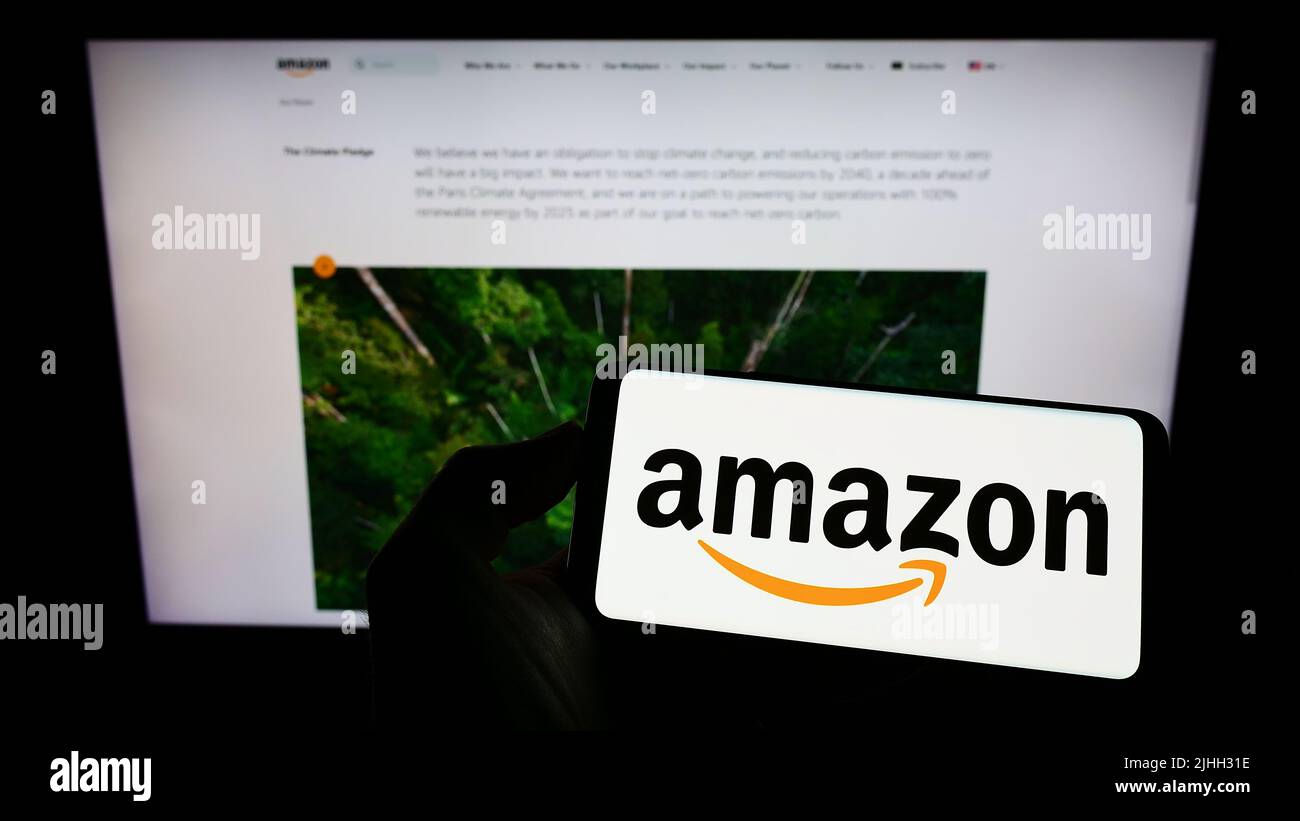 Person, die Mobiltelefon mit dem Logo des US-Technologieunternehmens Amazon.com Inc. Auf dem Bildschirm vor der Geschäftswebseite hält. Konzentrieren Sie sich auf die Telefonanzeige. Stockfoto