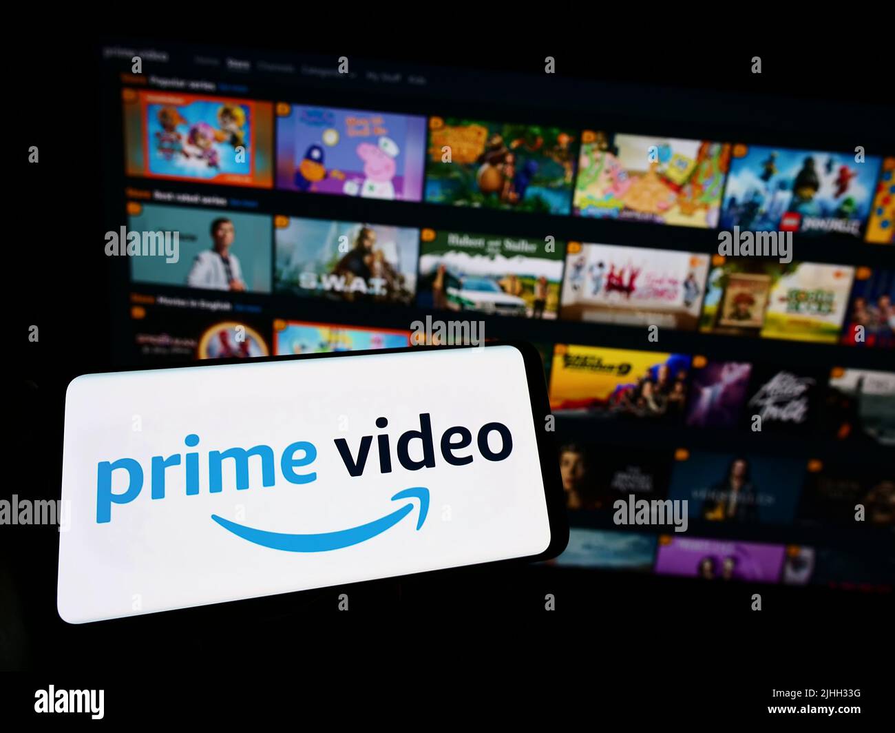 Person, die Mobiltelefon mit dem Logo des US-Streaming-Dienstes Amazon Prime Video auf dem Bildschirm vor der Business-Webseite hält. Konzentrieren Sie sich auf die Telefonanzeige. Stockfoto