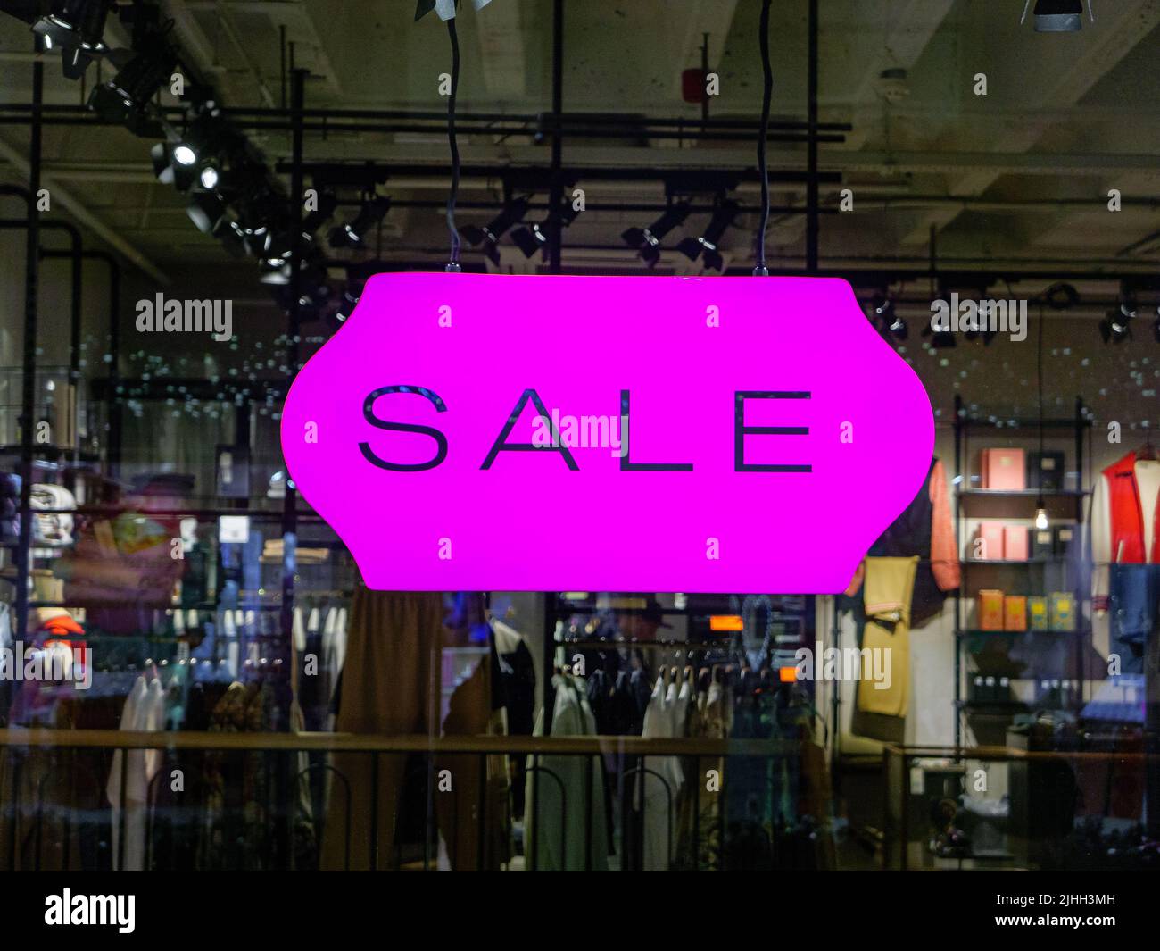 „Verkauf“-Schild in einem Schaufenster. Inneneinrichtung eines zufältigen Tuchladens auf dem Hintergrund (verloschter Hintergrund) Stockfoto